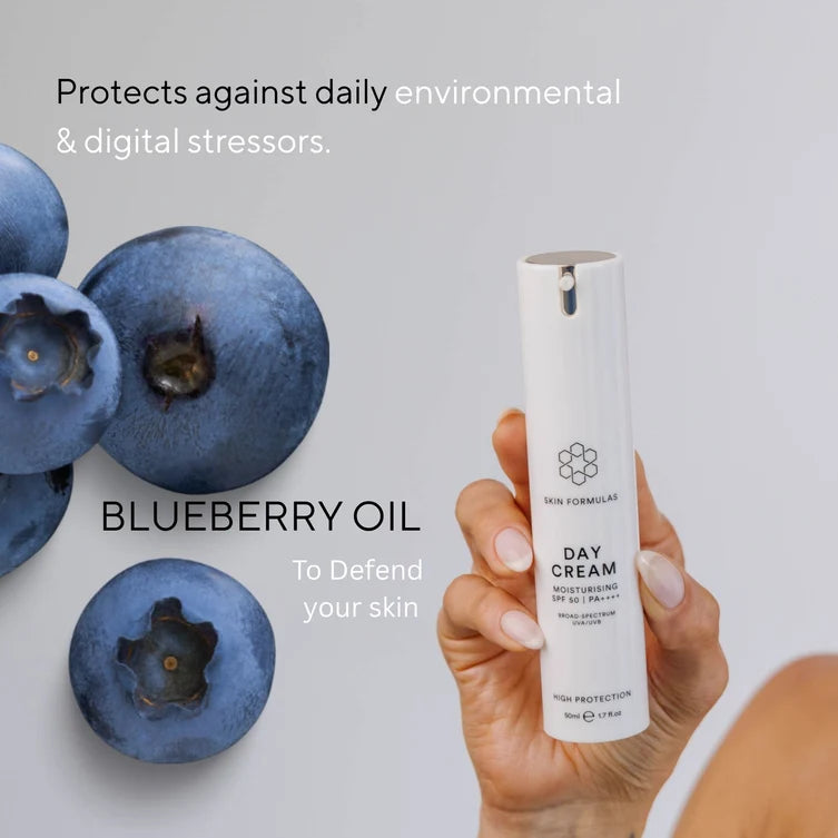 Day cream bottle held by a hand with blueberries on a light gray background