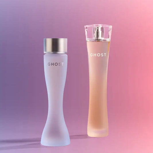 Two elegant Ghost perfume bottles on a soft pink-to-purple gradient background. One bottle is frosted white with a metallic silver cap, and the other is a translucent peach-pink bottle with a clear cap and spray nozzle.