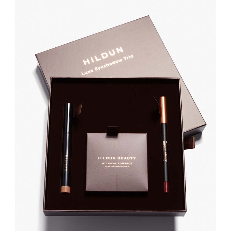 Hildun Beauty Luxe Eyeshadow Trio gift set in a dark brown box, containing a black eyeshadow stick with a bronze tip, a black pencil with a copper tip, and a matching eyeshadow compact.