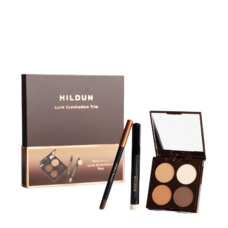 Hildun Luxe Eyeshadow Trio makeup set on a white background, including a brown and gold outer box, a four-pan eyeshadow palette, an eyebrow pencil, and a black eyeliner pencil.