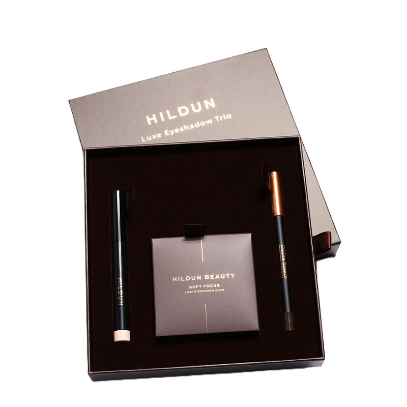 Hildun Luxe Eyeshadow Trio gift set in a dark brown box, containing a soft focus eyeshadow compact, a black eyeliner pencil with a rose gold tip, and a black eyeshadow pencil with a gold tip.