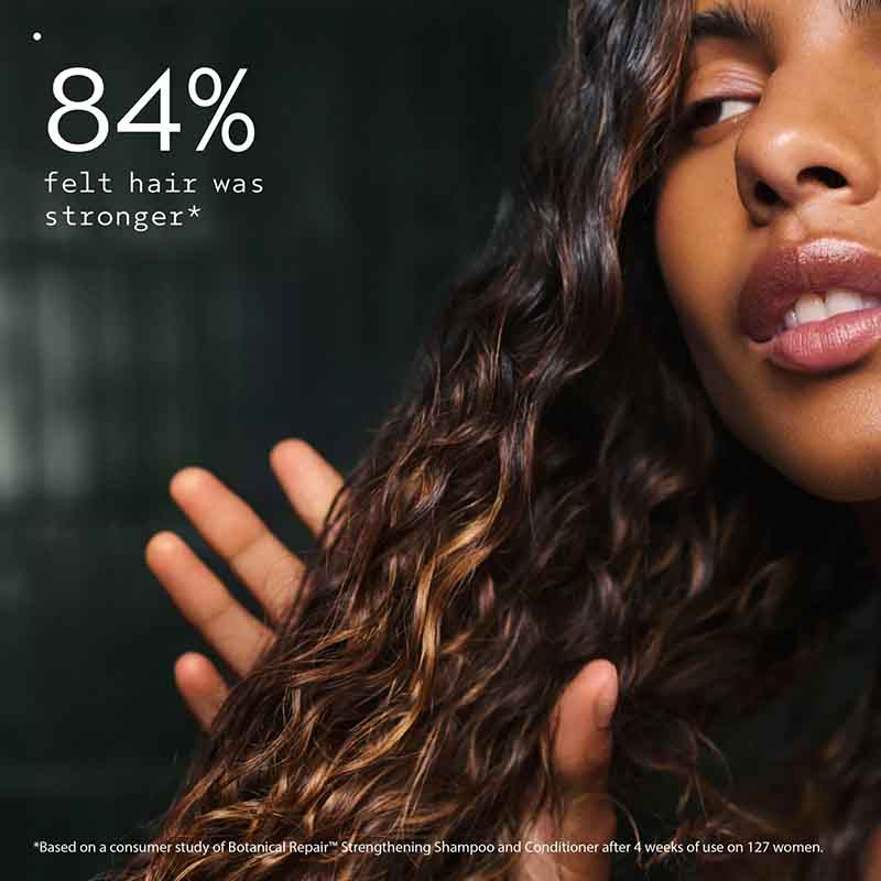 Close-up of a woman with long, wavy brown hair touching it, with text reading '84% felt hair was stronger*' on a dark background.