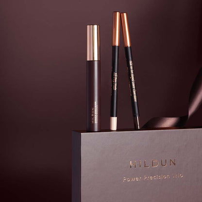 Hildun Power Precision Trio makeup set featuring a dark brown mascara tube and two matching eyebrow pencils with rose gold and black barrels, displayed on top of a dark brown Hildun gift box.