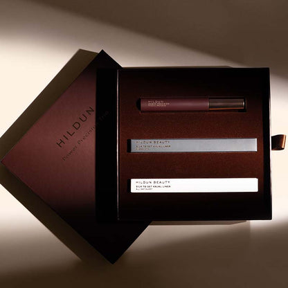 Hildun Beauty Power Reviver Mask set in a dark brown box, featuring a lip gloss tube, a silver mask tube, and a white sheet mask, with the brand's outer box visible beside it on a warm beige background.