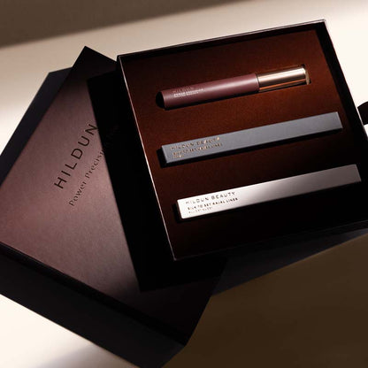 Hildun Beauty Power of Youth makeup set in a dark brown box, featuring a mauve lip product and two silver cosmetic tubes, with the branded box lid placed beside it.