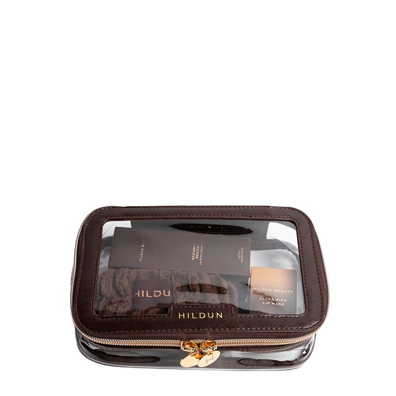 A Hildun cosmetic pouch in dark brown faux leather with a clear window showing makeup items inside, featuring a gold-tone zipper and logo on a white background.