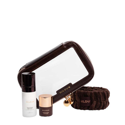 Hildun travel set featuring a brown faux-leather and clear window zippered pouch, a brown hair tie, and two skincare bottles (radiant serum and face primer) on a white background.