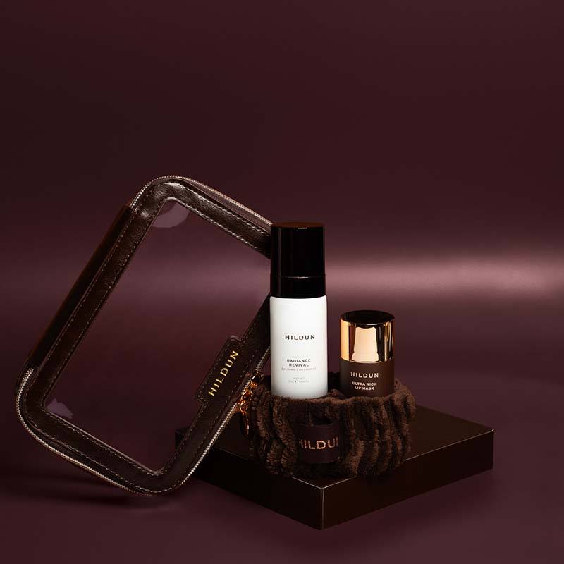 Mildun skincare set featuring a white and black serum bottle, a dark brown jar with a gold lid, and a brown textured pouch, arranged on a dark display stand against a deep plum background.
