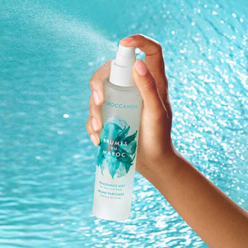 Moroccanoil Brumes du Maroc Hair and Body Mist being sprayed with bright turquoise be water behind the product