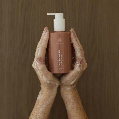Skin Formulas Hand Wash in hands with suds, a faint wooden background, the product is sitting in between the palm of both hands