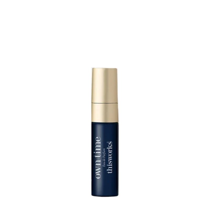 A small cylindrical cosmetic bottle with a dark navy blue body and a metallic gold cap, featuring white text that reads 'own time for thisworks' on a plain white background.